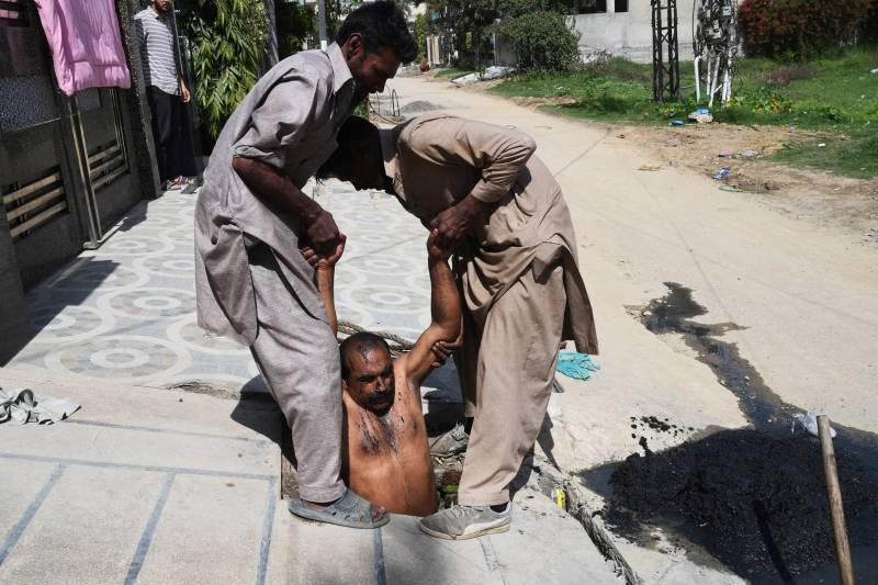 Sanitation worker Shafiq Masih (C) cleans a sewer with the help of colleagues in a residential area in Lahore. AFP