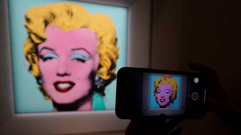 (FILES) In this file photo taken on March 21, 2022 a journalist takes photos of Andy Warhol’s 1964 ‘Shot Sage Blue Marilyn.’during a press preview in New York.