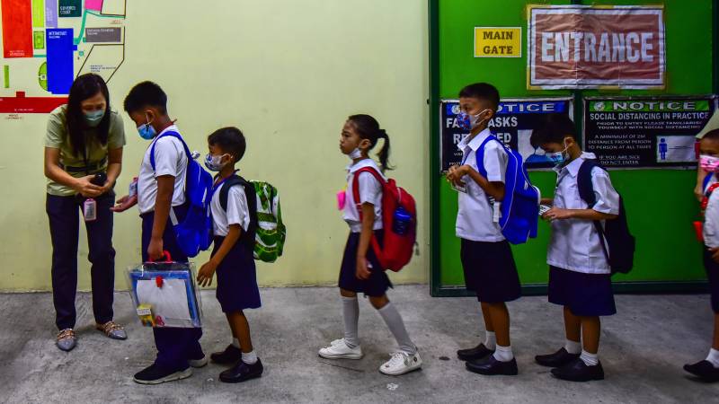 A teacher uses hand sanitizer on a student on the first day of in-person classes after years-long Covid-19 lockdowns at Pedro Guevara Elementary School in Manila. AFP