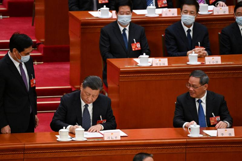 China's President Xi Jinping (C) signs a presidential order to appoint the new lineup of the State Council as Premier Li Qiang (R) looks on during the fifth plenary session of the National People's Congress (NPC) at the Great Hall of the People in Beijing on March 12, 2023. AFP