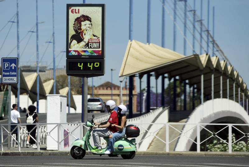 A couple ride a Vespa motorcycle past a street thermometer reading 44 degrees Celsius in Seville. AFP