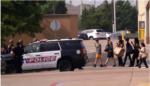 People raise their hands as they leave a shopping center after the shooting Saturday.